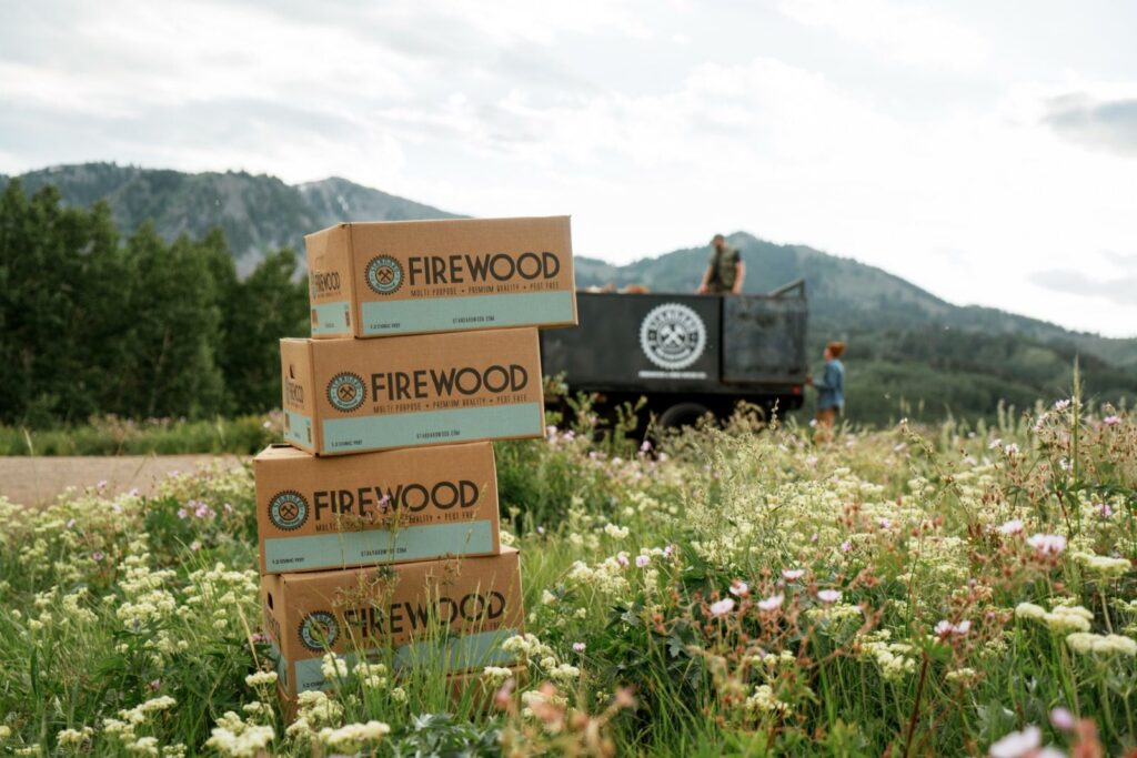 Stacked Standard Firewood boxes in a wildflower field near Park City, Utah, with a logo trailer and mountains behind