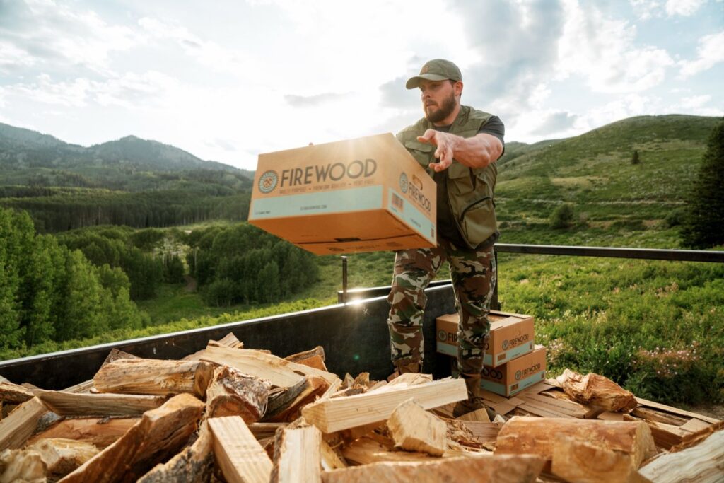 Worker tossing a Standard Firewood box from a trailer loaded with split firewood near Park City, Utah