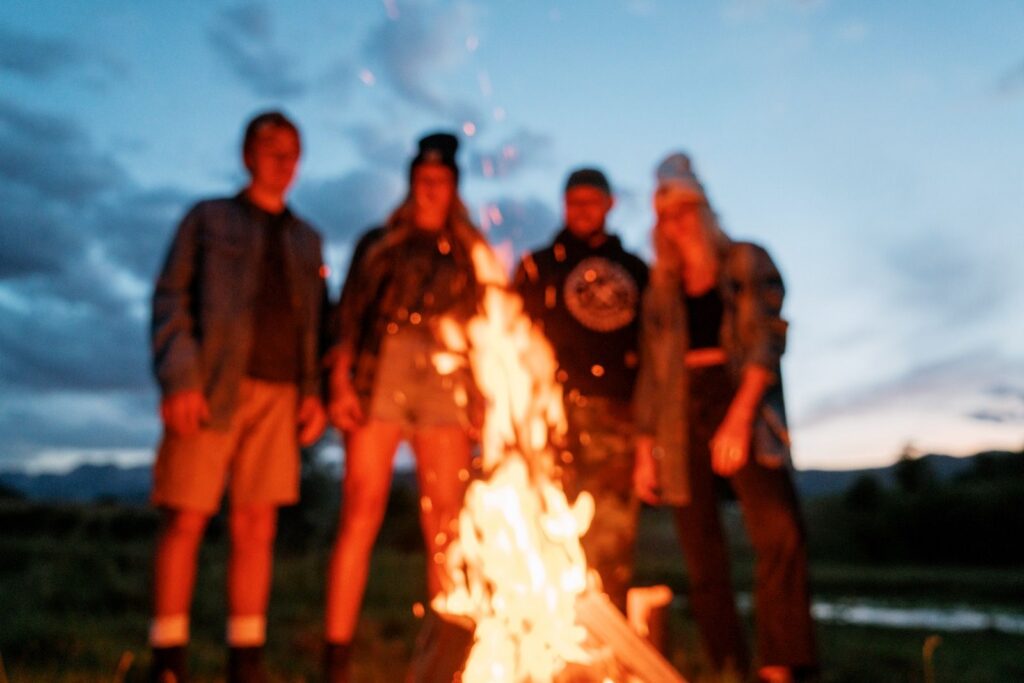 Four people standing around a campfire at dusk